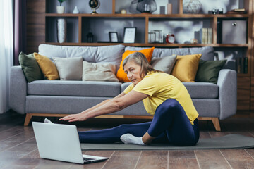 Senior woman doing fitness, sitting on the floor at home, using laptop for online sports group activities