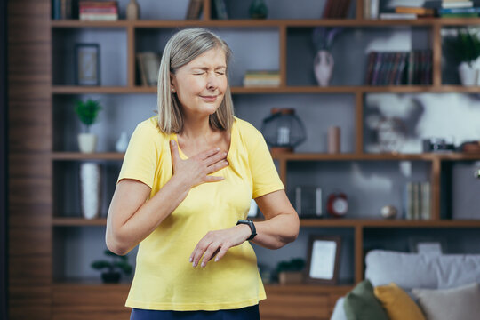 Older Woman At Home Doing Fitness Has Severe Shortness Of Breath And Chest Pain, Compares Bullets On Fitness Bracelets