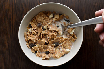 Fruit and fibre cereal with milk in a white bowl.  Healthy breakfast concept.  Cereal with wholewheat, dried fruit, raisin, coconut, banana, apple and hazelnuts. 