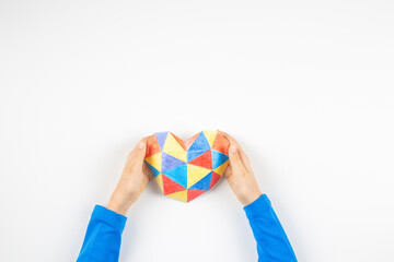Child hands holding colorful paper heart over multicolored paper background. World autism awareness day concept