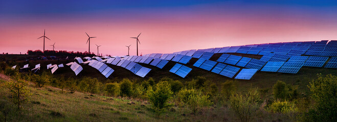 panoramic view of photovoltaic panels and wind turbines in the light of the rising sun, clean...