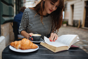 Charming woman reading book and drinking coffee at cafe