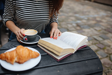Young woman sitting at cafe table with coffee and book