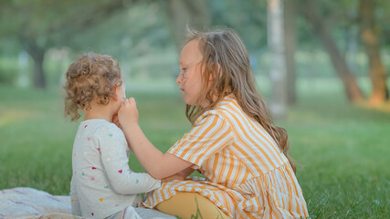 Two girls paint each other's faces at a picnic in the park