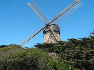 2009 Dutch Windmill at Golden Gate Park sits atop textured greenery covered hillside against bright...