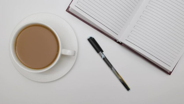 A businessman's workplace. A notepad, a ballpoint pen and a cup of hot coffee. Shooting from the top point. White background. Close-up.