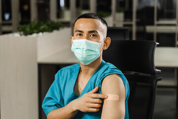 Handsome asian man vaccinated against coronavarus and showing patch on his arm. Covid-19 vaccination. Filipino man in medical mask