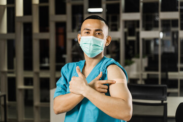 Fototapeta na wymiar Handsome asian man vaccinated against coronavarus and showing patch on his arm. Covid-19 vaccination. Filipino man in medical mask