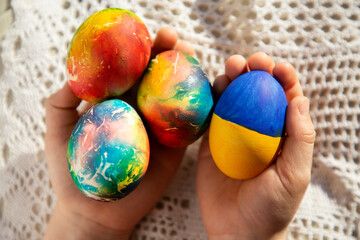 children's hands hold chicken eggs, one of which is painted in yellow-blue colors of the Ukrainian flag