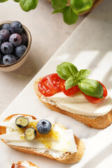 Italian antipasto bruschetta - white bread slices with smoked ham, goat cheese, blueberries, mozzarella, tomatoes, basil on marble board, glass with lemon water
