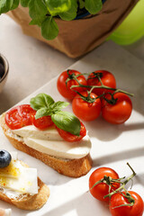 Italian antipasto bruschetta - white bread slices with smoked ham, goat cheese, blueberries, mozzarella, tomatoes, basil on marble board, glass with lemon water