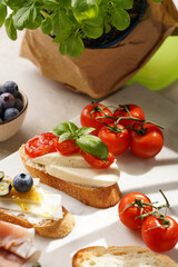 Italian antipasto bruschetta - white bread slices with smoked ham, goat cheese, blueberries, mozzarella, tomatoes, basil on marble board, glass with lemon water