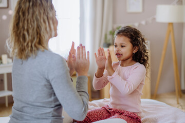 Happy mother with her little daughte playing clapping hands game on bed at home.