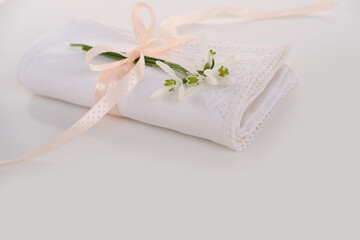 white linen napkin, finished with handmade lace, rolled in several layers, a delicate snowdrop flower is on a light table, the concept of luxury setting, a spring gift