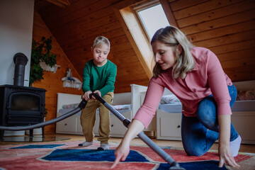 Boy with Down syndrome with his mother vacuum cleaning at home