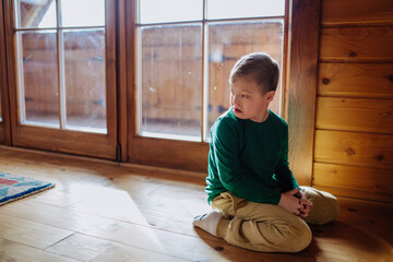 Sad little boy with Down syndrome sitting on floor at home.
