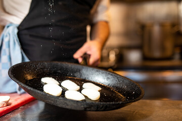 Cook preparing scallops in the kitchen with salt