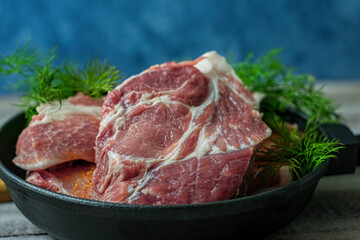 Close-up photo of cuts of meat with dill greens in a steak pan on wooden table with blue background