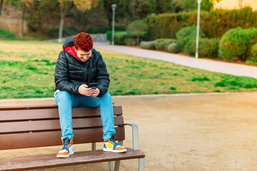 General shot of a modern woman with short red hair, non-binary, looking at her social networks in a public park.