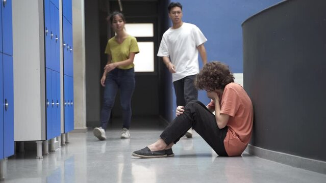 Sad teenager student sitting alone on floor victim of bullying and nice classmate friends help and console him. Empathy and support in Education
