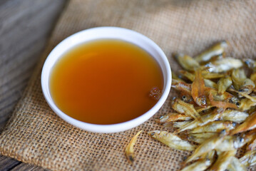 fish sauce on white bowl and small dried fish on sack, fish sauce obtained from fermentation fish or small aquatic animal, fermented foods