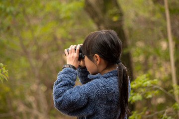春の森の中で双眼鏡を使って野鳥を観察している子供