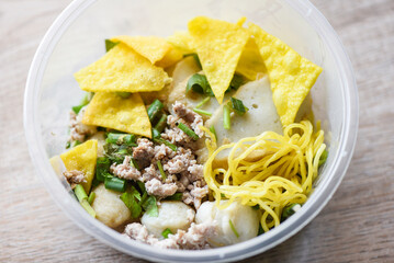 dry noodles pork balls fish balls and minced pork with crispy wontons and vegetable in plastic bowl on wooden table, top view Thai and China Asian food delivery concept