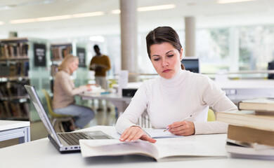 Adult female student with laptop and books in public library. High quality photo