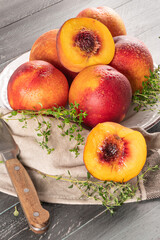 Naklejka na ściany i meble Ripe peaches with thyme leaves in a plate on a wooden board on a background