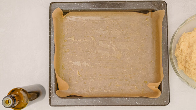 Baking pan covered with parchment paper, olive oil, and pizza dough. Close up baking process, flat lay