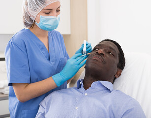 Fototapeta premium African american man getting injections for face skin tightening at aesthetic cosmetology clinic