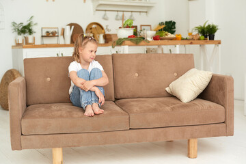A little girl is sitting on the couch at home and is sad. Domestic violence and abuse concept