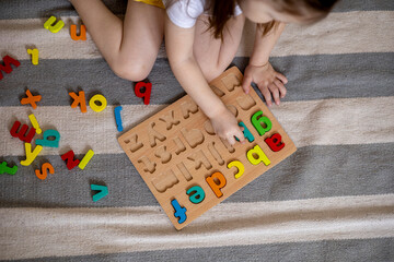 Top view of kids hands building words by using colored Montessori movable alphabet from the wooden tray on blackboard.
