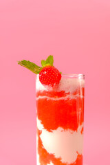 Strawberry cocktail with cream.Berry smoothies. Pink cocktail and cream in a transparent glass goblet with strawberries and sprigs of mint on a pink background.