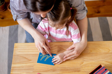 Montessori material. Mom helps her daughter learn letters using the rough alphabet. - obrazy, fototapety, plakaty