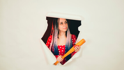Young woman with baseball bat in hole of white background. Pretty lady with bat.