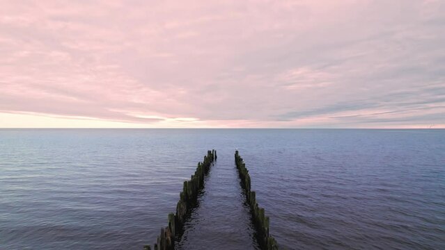 Flight of a drone over a wooden breakwater, green and destroyed by old age, which is installed in the Gulf of Riga in Jurmala, Sunset is blue-pink, the sun is not visible