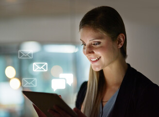 All my emails in the palm of my hand. Shot of a happy young designer using her tablet while working late in the office.