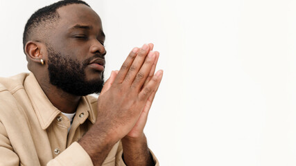 A black Muslim man prays while sitting on a couch. Web-banner