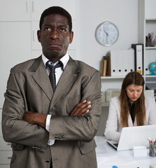 Portrait of upset businessman standing in office with working colleague behind