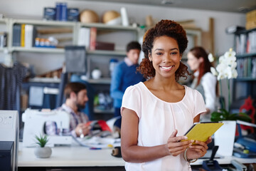 Im happiest with my designs in hand. Portrait of a young fashion designer standing in the workshop while her colleagues work in the background.