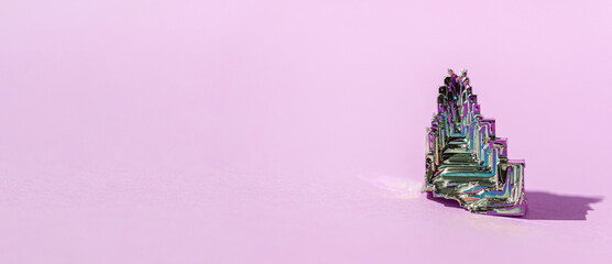 Synthetic bismuth Bismuthum crystal with iridescent oxide film on pink background close up...