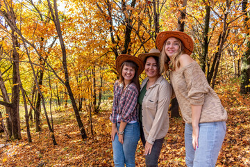 Naklejka na ściany i meble Three diverse female friends in cowboy hats are standing in the autumn forest.