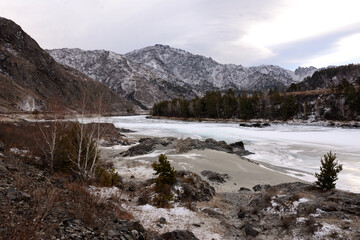 Rocky shore of an ice-bound river surrounded by snow-capped mountains.