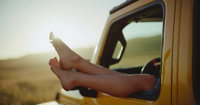 Relaxing on epic road trip, close up of feet hanging out the window of the car at sunset