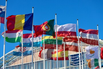 Group of EU memberstate flags waving in wind by EIB building in Luxembourg: Romania, Portugal, Poland, Austria, Hungary, Luxembourg, Lithuania, Latvia, Cyprus, Croatia, and Spain