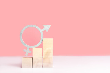 The concept of gender equality, mockup on a pink background with space for text. The symbol of gender equality in silver color stands on wooden cubes arranged in the form of a pyramid ladder.