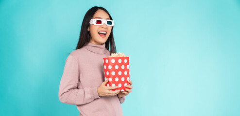 Young woman wearing 3d glasses with holding a red bucket of popcorns while looking movie on blue...