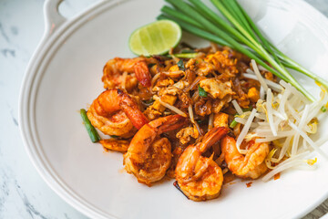 Shrimps Pad Thai or traditional Thai noodle menu, Pad Thai in stylish round shape white plate on marble table, close up image Thai food.