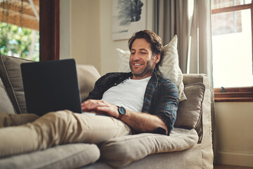 Im definitely not the leaving the house today. Shot of a handsome young man using his laptop while...